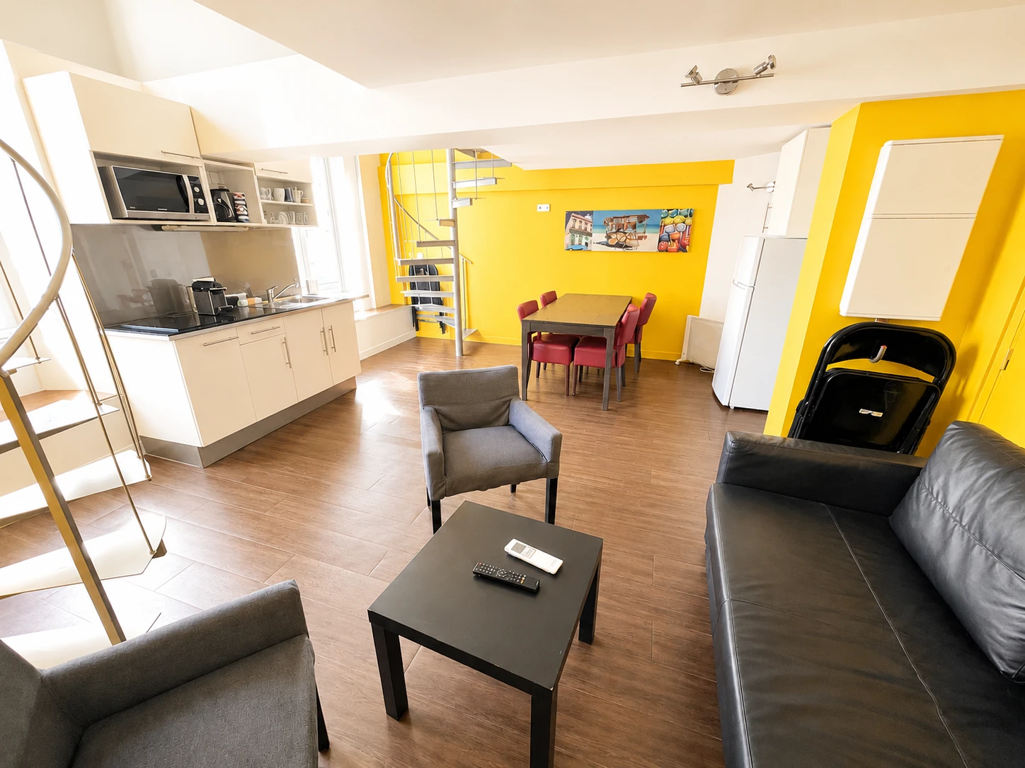 Overview of the living room and open-plan kitchen with yellow wall and spiral staircase – Grand Loft 3 Espaces, Carré d'Or Nice